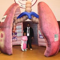 A young man wearing a white shirt and a black necktie and a little girl wearing a pink sweater stand in the middle of an inflatable model of a human lung.