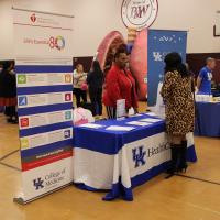 A woman attending the event speaks with a woman standing behind a table that's covered with a UK HealthCare blue and white tablecloth.