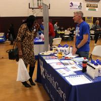 A woman attending the event speaks with a man standing behind a table that's covered with a UK HealthCare blue and white tablecloth.