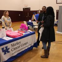 A group of people has a conversation around a table with a UK Markey Cancer Center tablecloth on it.