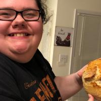 A close-up photo of Abby smiling while holding up a loaf of bread in the family’s kitchen.