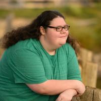 A photo of Abby leaning over the railing of a wooden bridge as she looks off into the distance.