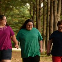 A candid photo of Jamie, Abby, and Drew walking together through a picturesque row of trees. Abby and Jamie are holding hands.