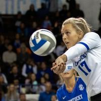 An action shot of Alli during a volleyball game, a millisecond after hitting a volleyball with her two hands held closely together. She is looking up and away, in the direction that the ball is going.