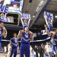 A shot of Allie and her fellow UK cheerleaders mid-performance at a UK men’s basketball game. The female cheerleaders are holding signs that read “We Are UK” while sitting on the shoulders of the male cheerleaders. All of the cheerleaders are in blue and white UK cheerleader uniforms.