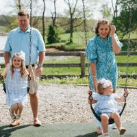 A candid photo of Anne Sydney and Jesse pushing their daughters on the swing set.