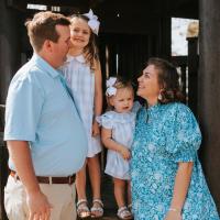 A candid photo of the Parrish family smiling at each other as they stand in front of a structure at the playground.