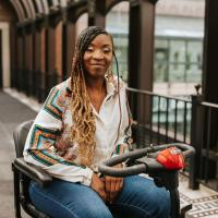 A photo of Brandi smiling for the camera while sitting on an electric scooter on the walkway of a skywalk.