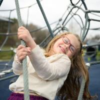 A close-up photo of Cate smiling as she leans back and holds onto a rope at the playground.