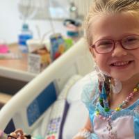 A close-up photo of Cate smiling in her hospital bed while wearing a princess dress.