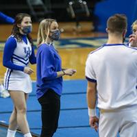 Coach O’Connor stands around her male and female cheerleading student athletes as they practice. All of them are wearing face masks.