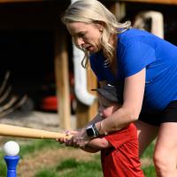 Coach O’Connor helps her son hold a toy bat and swings it towards the incoming ball.