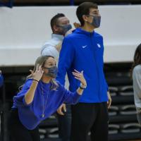 With her hands up in the air, Coach O’Connor passionately cheers and directs her team from the sidelines at a competition.