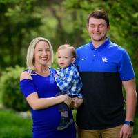 The O’Connor family stands outside together and smiles. Coach O’Connor is holding Michael, and her husband stands next to them.