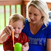 Coach O’Connor sits beside her toddler, Michael, on a patio. She is wearing a blue Kentucky shirt, and her son is wearing a red shirt.