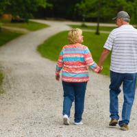 Danny and his wife, an older white woman with blonde hair, walk down a path at a park.