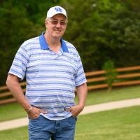 Danny stands and smiles with his hand placed in his pockets at the park.