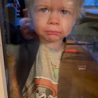 Kelsey’s two-year-old stands on the other side of a window, frowning with a teary-eyed expression.