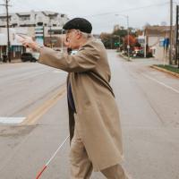 Donald is crossing the street using his cane, and points forward ahead of him.