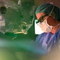 A profile view of Dr. Fraser as she performs surgery, surrounded by different machines in an operating room.