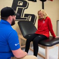 Donna sits on a patient's bench while her physical therapist talks to her about her knee.