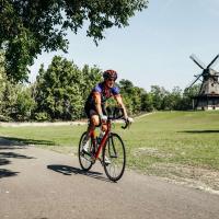 Doug rides his bike past a windmill in a rural outdoor setting.