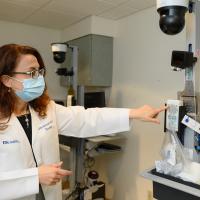 Dr. Bensalem-Owen stands in her lab, pointing at one of the brain computer interface tools used in recording brainwaves.