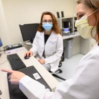 One of Dr. Bensalem-Owen’s colleagues, a white woman with long brown hair, points to a screen monitor of data.