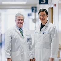 Dr. McLarney and Dr. Gurley wearing their white doctor's coats smile for a photo in a hallway at the hospital.