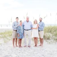 E and her family pose for a group photo on a sandy dune with long grass at the beach.