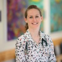 A photo of Dr. Eimear McGovern smiling for the camera while standing in front of artwork.