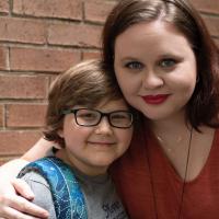 A photo of Ellie and her mom, Morgan, a young looking woman with brown hair wearing red lipstick and an orange shirt. Morgan’s arm is around Ellie’s shoulders. Both are smiling.