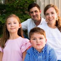 The Crittenden family, including parents Ben and Amy, dressed in white shirts, with their young daughter, Beatrice, in a pink shirt, standing beside their son, Elliott, dressed in a blue and white checkered shirt.