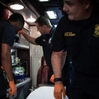 Three adult men in EMS uniforms standing in the back of an ambulance, checking the equipment surrounding them.