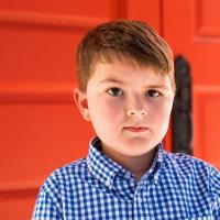 Elliott, a young boy in a blue and white checkered shirt, looking into the camera and slightly smiling.