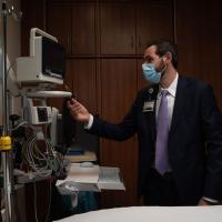 Chase wears a face mask and examines a monitor in a patient’s room.