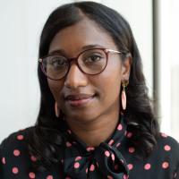 A portrait of Nakia Coffman, a young Black woman with black hair and round glasses, wearing a black blouse with pink polka-dots.