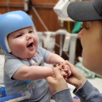 A candid photo of Claire gently playing with baby Everett, who is wearing a cranial helmet.