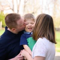 A photo of Claire and Daniel holding Everett while they each kiss Everett’s cheek.