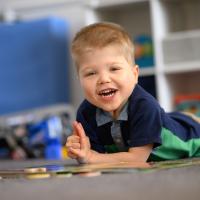 A close-up photo of Everett smiling for the camera as he lays on the floor with his toys.