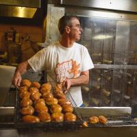 Fred takes a fresh batch of donuts off the glazing machine.