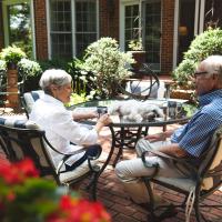 Gayle and her husband chat over coffee outside while their dog rests on a table.