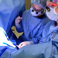 Dr. Amanda Saltzman and a surgical technician, both dressed in light blue scrubs, practicing techniques on an operating table.