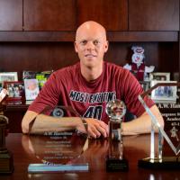 A.W. smiles for the camera while sitting at his desk, surrounded by trophies and family photos.