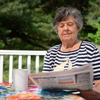 A candid photo of Helen reading the newspaper while sitting out on her back porch.