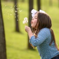 Henley stands in a park blowing a handful of dandelions.