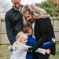 The Longeway family stand embraced together in an outside setting. Amongst them is Amy Longeway, a blonde white woman in a black cardigan, her husband, in a black sweatshirt, Henry in a blue sweatshirt and his younger sister in a grey sweatshirt.