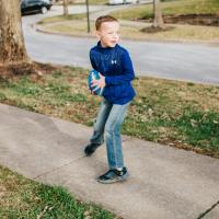 Henry stands on the pavement outside. He is about to throw a blue football and poses in the position to do so.