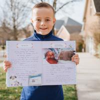 Henry stands outside with a big smile as he holds up a diary with writings and images from his experience as a baby.