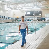 A photo of Jaida, dressed in a white t-shirt and blue track pants, walking alongside the pool.